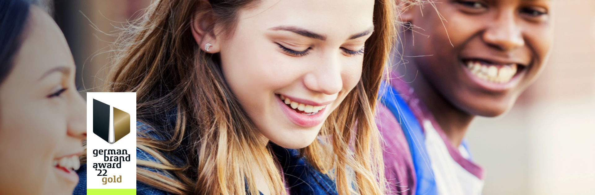 Three young people laugh together and appear relaxed – a symbol of positive user experiences with the berufswahlapp. On the left in the image is the logo of the German Brand Award 2022 in gold.