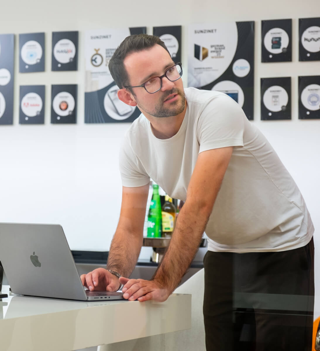 Ein Mann steht an einem Tisch und lehnt sich leicht nach vorne, während er an einem Laptop arbeitet | AI Chatbot SUNZINET