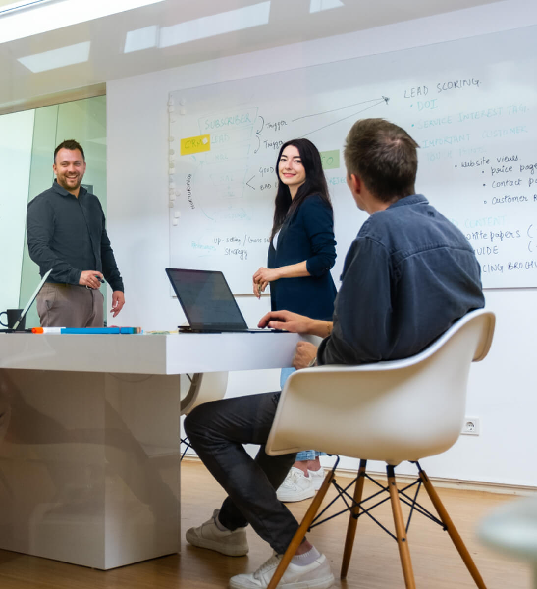 Eine Gruppe von drei Kollegen diskutiert in einem Besprechungsraum, mit einem Whiteboard voller Notizen im Hintergrund | AI Chatbot SUNZINET