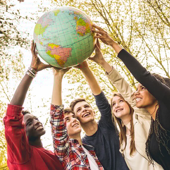eine Gruppe von fünf verschiedenen jungen Menschen, die im Freien stehen und gemeinsam eine Weltkugel halten. Sie alle lächeln und heben die Weltkugel mit beiden Händen über ihre Köpfe. Im Hintergrund sind Bäume mit grünen Blättern zu sehen, und die Gesamtatmosphäre wirkt positiv und geeint. | content optimierung SUNZINET