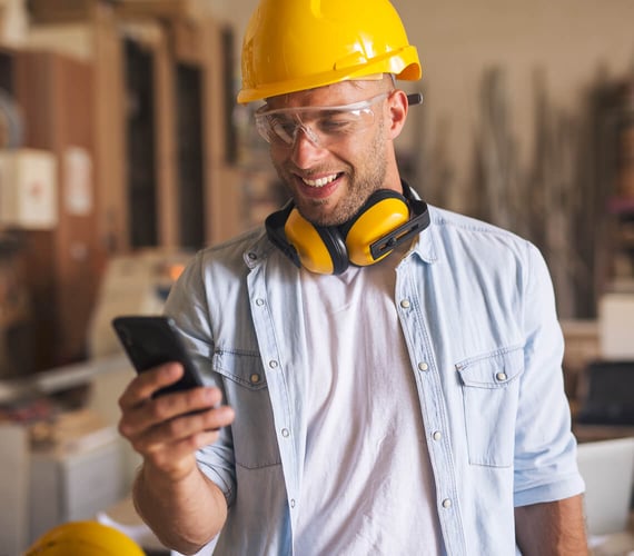Man wearing a yellow hard hat, hearing protection, and a blue shirt over a white T-shirt looks at his smartphone – Nevaris 123erfasst market entry in Poland – Go-to-market strategy – SUNZINET digital agency