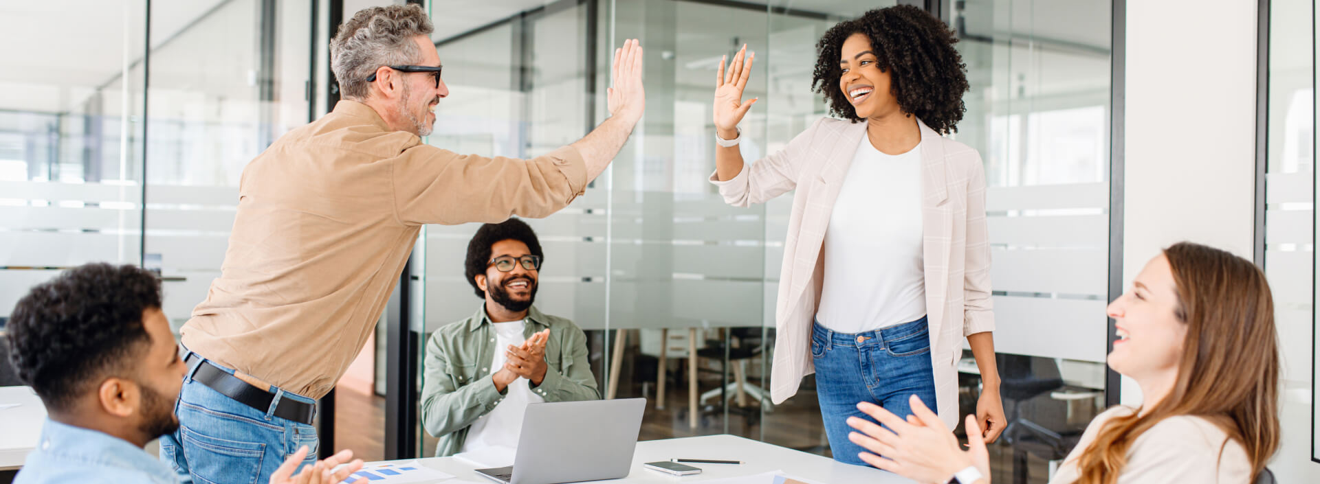 eine Gruppe von Kollegen in einer modernen Büroumgebung, die einen Erfolg feiern. Ein Mann gibt einer Frau ein High-Five, während zwei andere im Hintergrund klatschen und lächeln. | innovationskultur SUNZINET