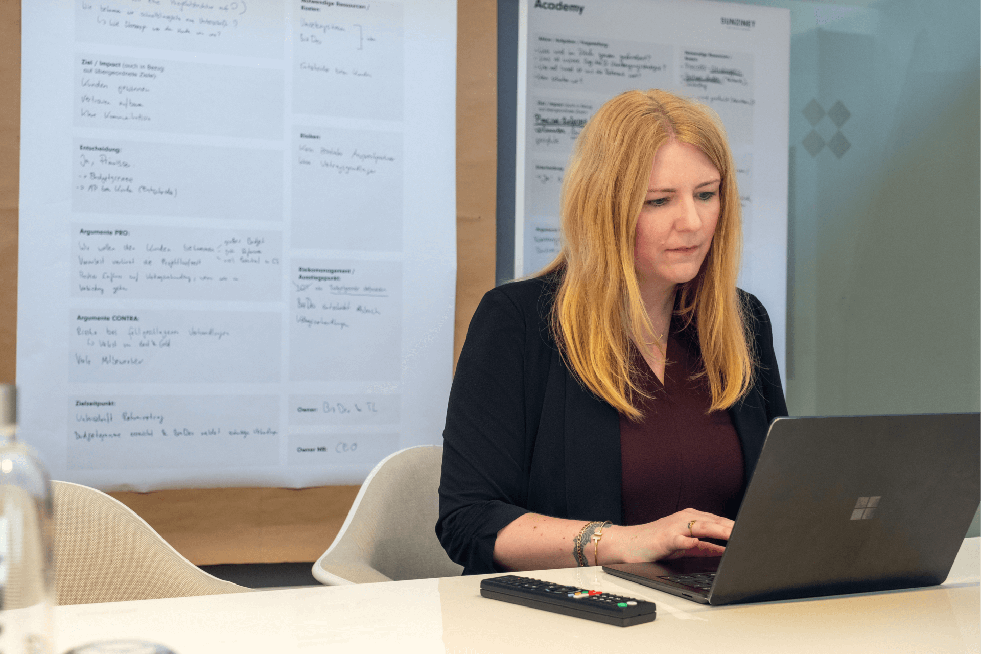 Frau, die während eines Workshops oder einer Strategiesitzung konzentriert an einem Laptop arbeitet, mit handgeschriebenen Planungsvorlagen an der Wand hinter ihr | social-media-marketing strategien SUNZINET
