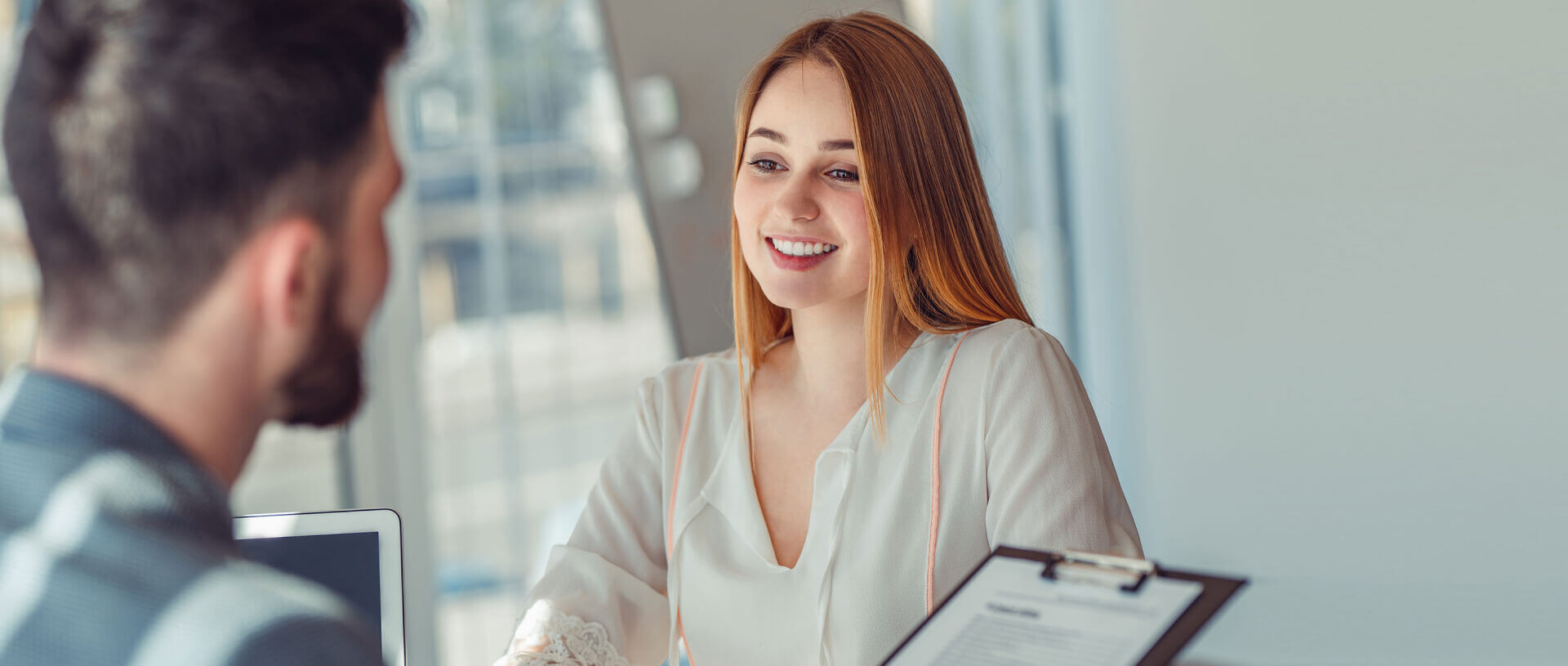 Professional business meeting between a young woman with long red hair, smiling, and a man with short dark hair, partially visible from behind | Salesforce UX optimization SUNZINET
