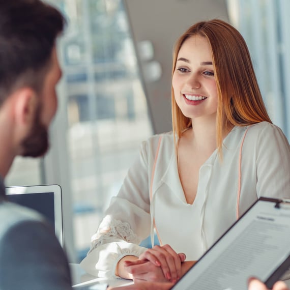 Professionelle Umgebung, in der eine lächelnde Frau mit langen, glatten roten Haaren in ein Gespräch mit einem Mann vertieft ist | Salesforce UX-Optimierung SUNZINET