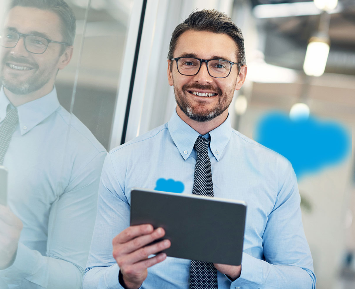 Ein Mann mit Brill und blauem Hemd schaut lachend in die Kamera, dabei hält er ein Tablet. Salesforce Logo.