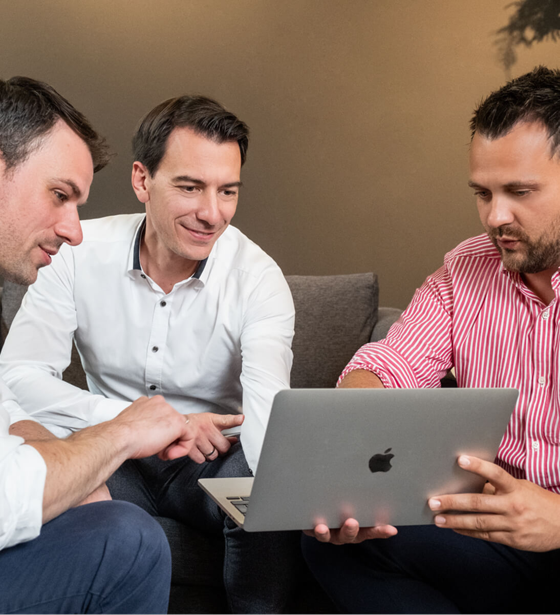 Drei Männer sitzen sich gegenüber und schauen gemeinsam auf einen Laptop. | KI-Integration von SUNZINET
