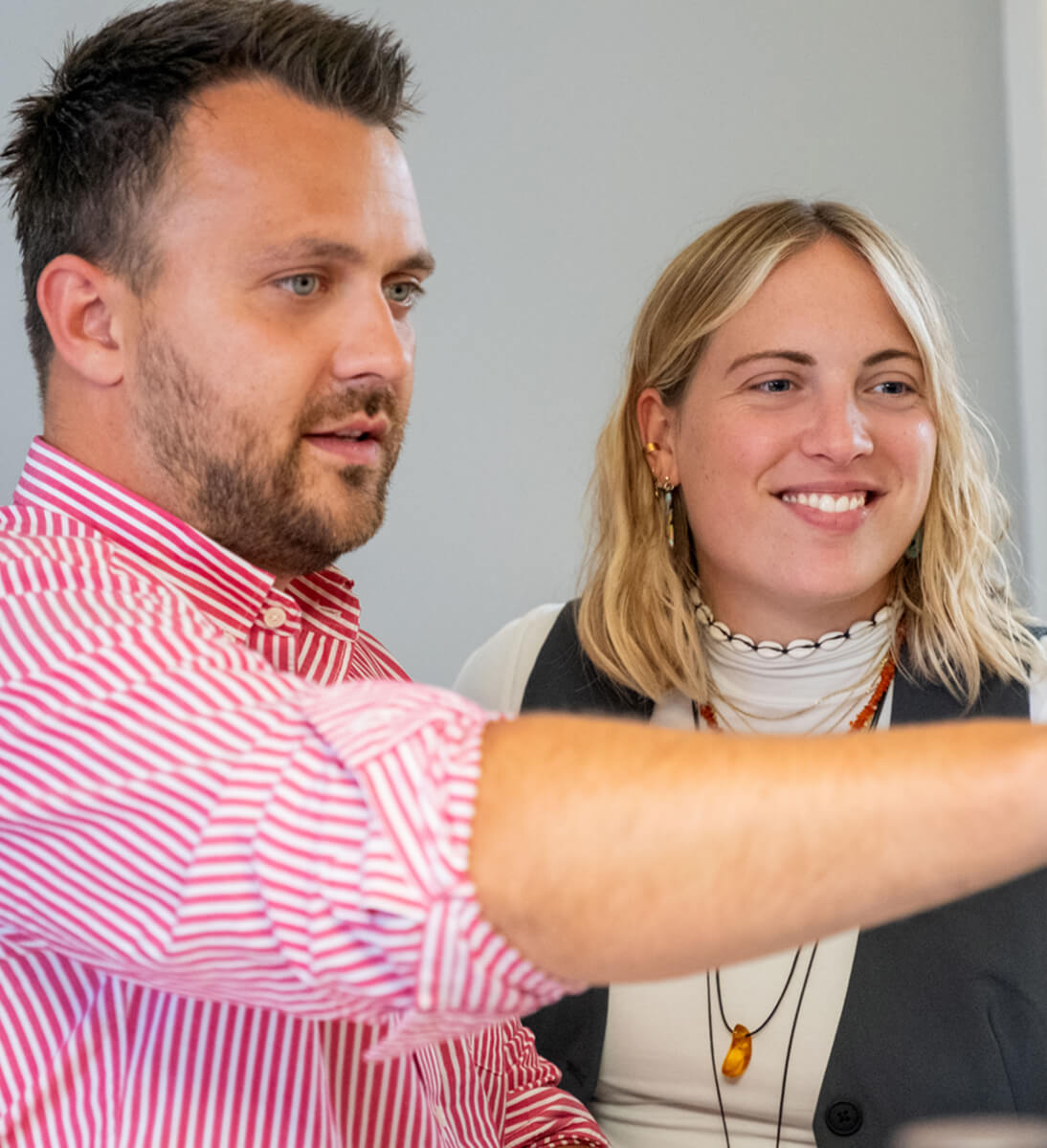 Ein Mann und eine Frau arbeiten gemeinsam an einem Computerbildschirm, lächelnd und mit der Aufgabe beschäftigt. Der Mann trägt ein rot-weiß gestreiftes Hemd, die Frau hat kurze blonde Haare und trägt ein weißes Hemd mit einer Halskette | Interne Kommunikation SUNZINET
