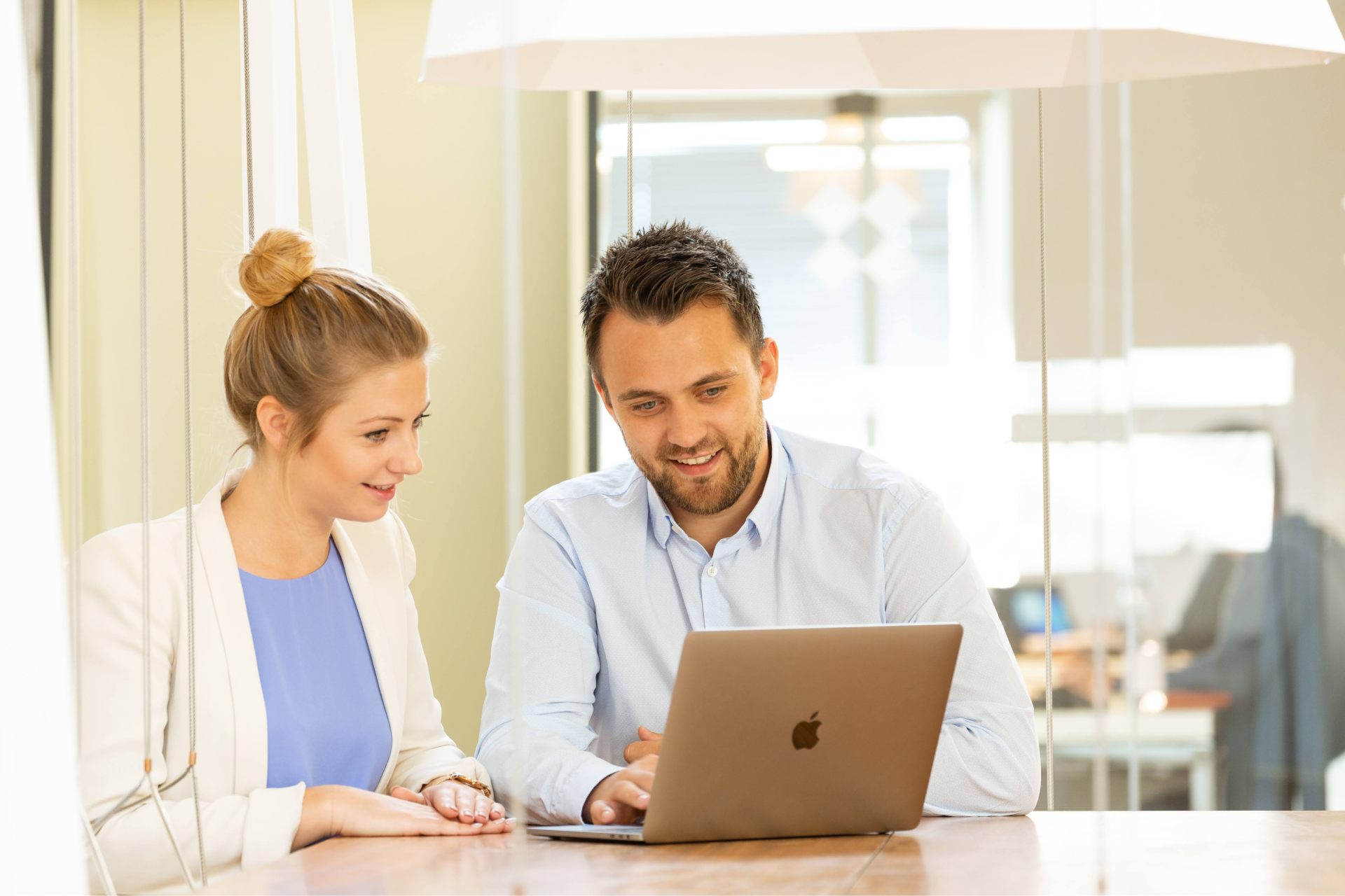 Mann und Frau, Mitarbeiter von Sunzinet, schauen lächelnd gemeinsam im Büro auf Daten am Laptop