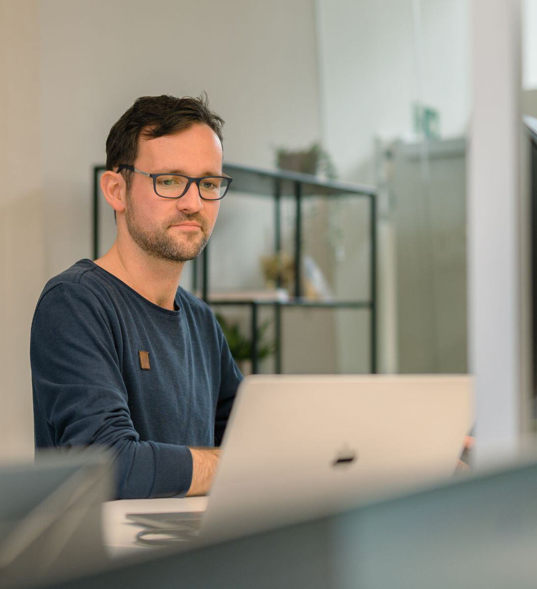 Ein Mann sitzt an einem Tisch und arbeitet an einem Laptop. Im Hintergrund sind Regale zu sehen. KI-Beratung von SUNZINET