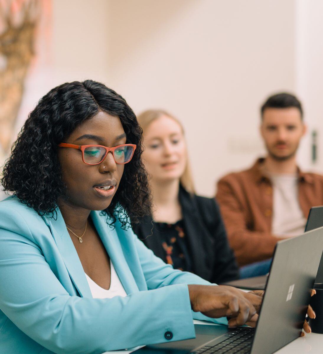 Frau erklärt zwei Personen etwas am Laptop
