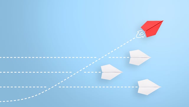 A red paper airplane leading a group of white paper airplanes, with dashed lines showing their flight paths, symbolizing innovation and leadership | management of change process SUNZINET