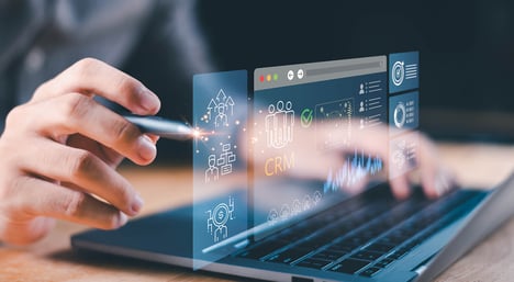 Nahaufnahme einer Person, die mit einem Stylus auf einem Laptop arbeitet, auf dessen transparentem digitalen CRM-Bildschirm Kundendaten, Analysen, Diagramme und Symbole zur Unternehmensführung angezeigt werden.  | Customer Platform-Agentur SUNZINET