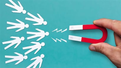 Eine Hand hält einen rot-weißen Hufeisenmagneten, der auf mehrere stilisierte weiße Papierfiguren gerichtet ist. Die Figuren werden durch gezackte Linien symbolisch vom Magneten angezogen. Der Hintergrund ist einfarbig türkis. Die Darstellung steht sinnbildlich für Kundenbindung.