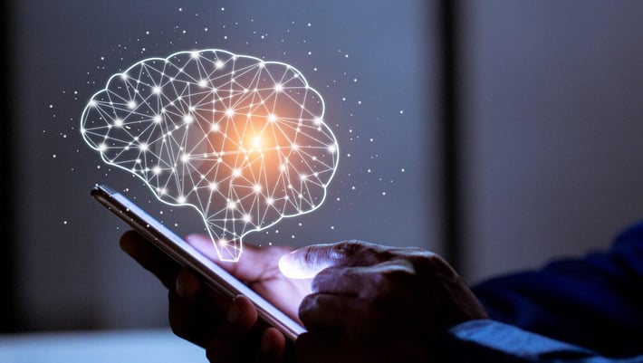Ein Benutzer hält ein Smartphone in der Hand, während über dem Gerät eine stilisierte Darstellung eines Gehirns in Form von leuchtenden, vernetzten Linien schwebt. Das Bild symbolisiert künstliche Intelligenz und digitale Innovation. | Voraussetzungen für KI
