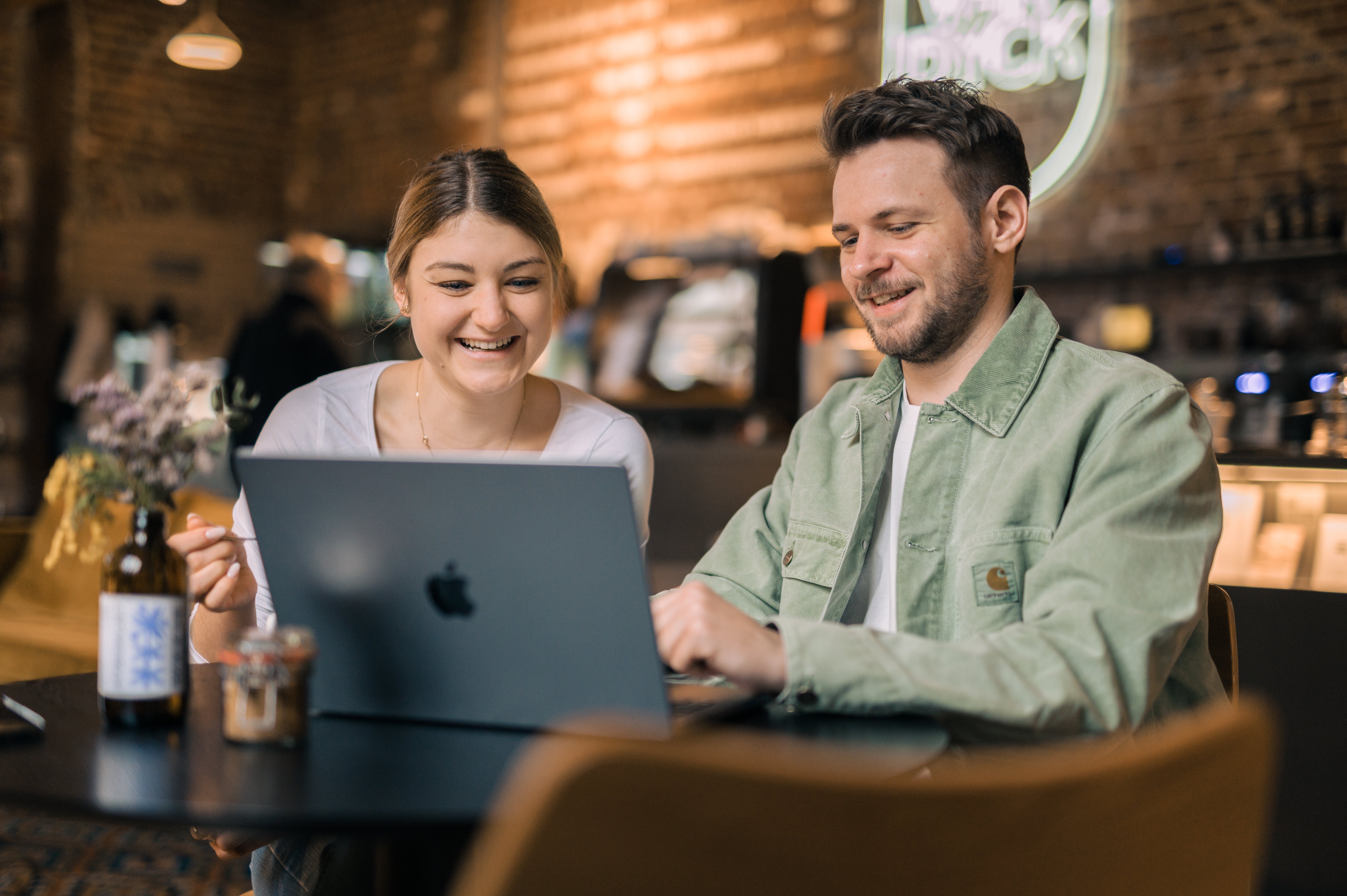 Zwei Kollegen sitzen in einem Café vor einem Laptop. 