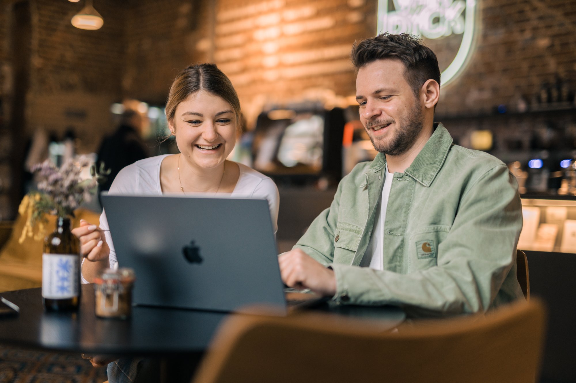 Zwei Kollegen sitzen in einem Café vor einem Laptop. 