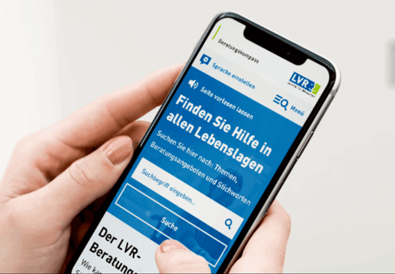 Eine Person hält ein Smartphone, das die Beratungsplattform von LVR zeigt. Auf dem Bildschirm steht 